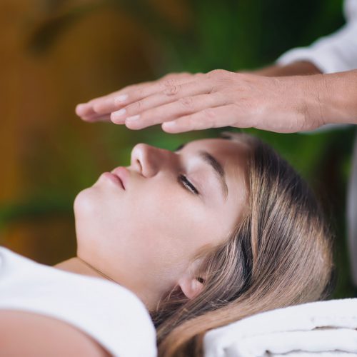 Horizontal image of Reiki therapist holding hands above head of the patient and transfer energy. Peaceful teenage girl lying with her eyes closed.